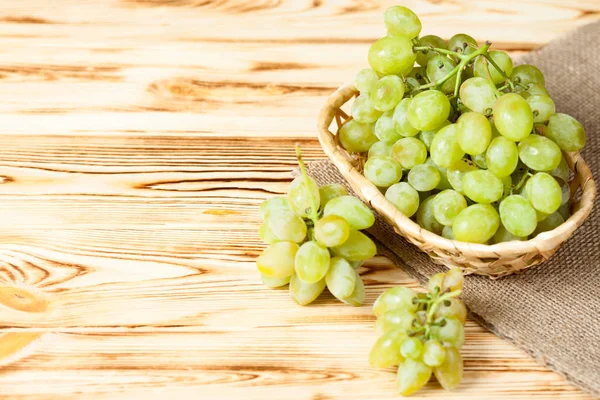 Demet taze olgun Yeşil üzüm ahşap dokulu arka plan üzerinde çul parçası üzerinde hasır sepet içinde. Yeşil üzüm bir dalı ile güzel arka plan. Kopya alanı ile Üstten Görünüm.