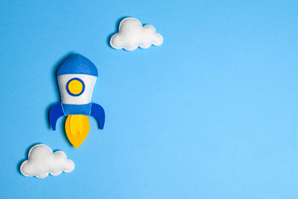 Rocket takes off. Space ship with white clouds on blue background. Hand made felt toys.