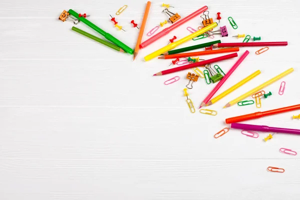Colorful pencils and felt-tip pens, paper clips, stationery nails, smilie binders on white wooden background