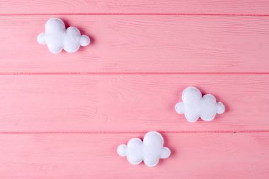 Çerçeve, pembe ahşap zemin üzerine boşaltmak ile zanaat beyaz bulutlar. El yapımı keçe oyuncak. Soyut gökyüzü.
