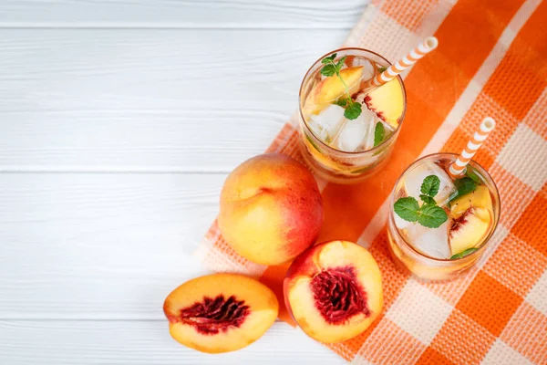 Buz ve nane yaprakları ile şeftali limonata. Ev yapımı limonata, beyaz ve turuncu olgun olgun nektarin. Şeftali çay iki kadeh. Beyaz ahşap zemin üzerinde serinletici yaz içeceği.