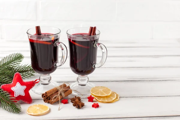 Winter horizontal mulled wine banner. Glasses with hot red wine and spices, tree, felt decorations on wooden background.