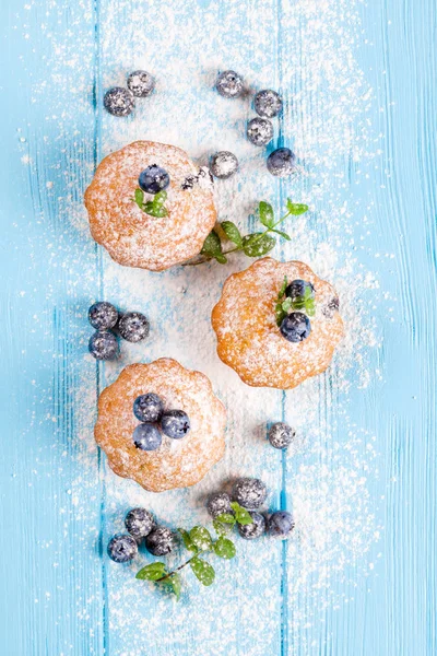 Blueberry muffin. Homemade baked cupcake with blueberries, fresh berries, powdered sugar on blue wooden background. Top view.