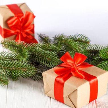 Beyaz ahşap zemin üzerinde kırmızı kurdele ve yay, yeşil Noel ağacı süslemeleri ile el sanatları Hediyelik kutu. Noel ve yeni yıl kutlama kartı, afiş, el ilanı.