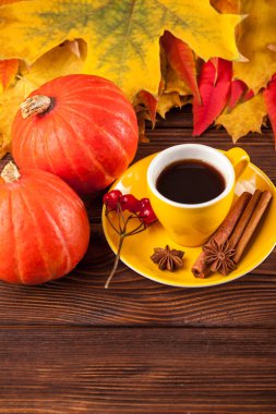 Sonbahar dikey afiş sarı ile kırmızı yaprakları, pumpkins, fincan kahve ve guelder gül kahverengi ahşap zemin üzerinde.