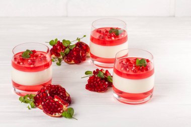 Güzel gözlük kırmızı jöle, Beyaz ahşap zemin üzerinde taze olgun Nar ile kremsi vanilya panna cotta.