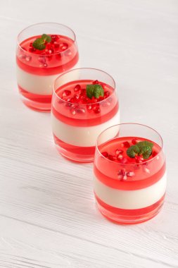 Güzel gözlük kırmızı jöle, Beyaz ahşap zemin üzerinde taze olgun Nar ile kremsi vanilya panna cotta.