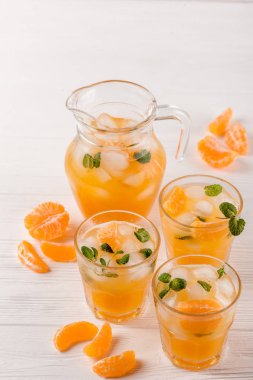 Mandarin buz ve güzel gözlük ve sürahi, Beyaz ahşap zemin üzerinde olgunlaşmış taze narenciye nane kokteyli. Tatlı portakal suyu. Fotoğraf kadar kapatın. Seçici odak