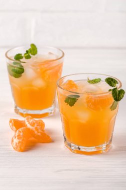 Mandarin buz ve güzel gözlük ve sürahi, Beyaz ahşap zemin üzerinde olgunlaşmış taze narenciye nane kokteyli. Tatlı portakal suyu. Fotoğraf kadar kapatın. Seçici odak