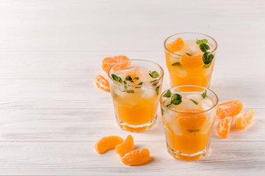 Mandarin buz ve güzel gözlük ve sürahi, Beyaz ahşap zemin üzerinde olgunlaşmış taze narenciye nane kokteyli. Tatlı portakal suyu. Fotoğraf kadar kapatın. Seçici odak