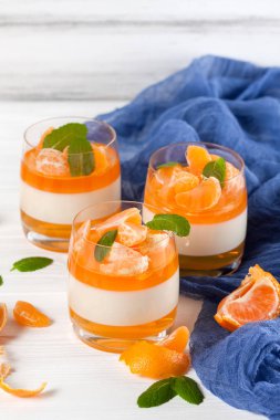 Güzel gözlük, taze olgun mandarin, Beyaz ahşap zemin üzerinde mavi tekstil turuncu jöle ile kremsi panna cotta. Lezzetli İtalyan tatlı. Portre fotoğrafçılığı. Seçici odak.