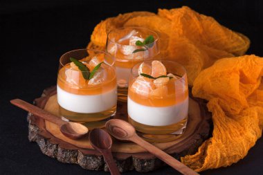 Kremsi panna cotta ile güzel bardaklarda portakal jöle, taze olgun mandarin siyah arka plan üzerine ahşap bölümünde. Lezzetli İtalyan tatlı. Modern karanlık ruh stili.