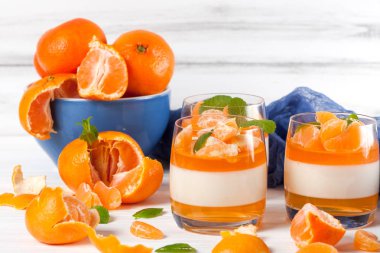 Güzel gözlük, taze olgun mandarin, Beyaz ahşap zemin üzerinde mavi tekstil turuncu jöle ile kremsi panna cotta. Lezzetli İtalyan tatlı. Portre fotoğrafçılığı. Seçici odak.