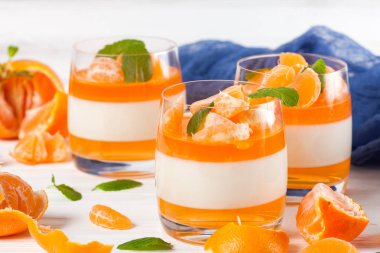 Güzel gözlük, taze olgun mandarin, Beyaz ahşap zemin üzerinde mavi tekstil turuncu jöle ile kremsi panna cotta. Lezzetli İtalyan tatlı. Portre fotoğrafçılığı. Seçici odak.