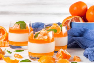 Güzel gözlük, taze olgun mandarin, Beyaz ahşap zemin üzerinde mavi tekstil turuncu jöle ile kremsi panna cotta. Lezzetli İtalyan tatlı. Portre fotoğrafçılığı. Seçici odak.