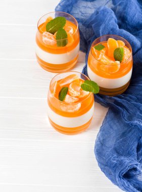 Güzel gözlük, taze olgun mandarin, Beyaz ahşap zemin üzerinde mavi tekstil turuncu jöle ile kremsi panna cotta. Lezzetli İtalyan tatlı. Portre fotoğrafçılığı. Seçici odak.