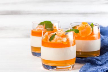 Güzel gözlük, taze olgun mandarin, Beyaz ahşap zemin üzerinde mavi tekstil turuncu jöle ile kremsi panna cotta. Lezzetli İtalyan tatlı. Portre fotoğrafçılığı. Seçici odak.