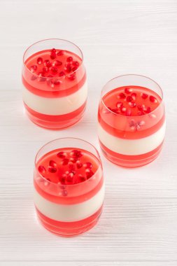 Güzel gözlük kırmızı jöle, Beyaz ahşap zemin üzerinde taze olgun Nar ile kremsi vanilya panna cotta.