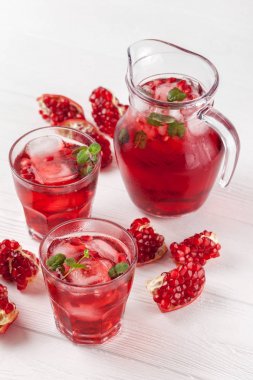 Nar buz ve güzel gözlük ve sürahi, taze olgun nar Beyaz ahşap zemin üzerine nane kokteyli. Tatlı kırmızı suyu. Fotoğraf kadar kapatın. Seçici odak