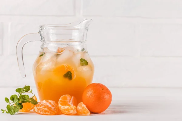 Cocktail al mandarino con ghiaccio e menta in bellissimi bicchieri e brocca, agrumi freschi maturi su fondo bianco in legno. Succo d'arancia dolce. Chiudi la fotografia. Focus selettivo — Foto Stock