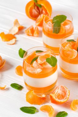 Kremsi panna cotta ile güzel bardaklarda portakal jöle taze olgun mandalina, Beyaz ahşap zemin üzerinde. Lezzetli İtalyan tatlı. Portre fotoğrafçılığı. Seçici odak.