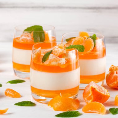Kremsi panna cotta ile güzel bardaklarda portakal jöle taze olgun mandalina, Beyaz ahşap zemin üzerinde. Lezzetli İtalyan tatlı. Portre fotoğrafçılığı. Seçici odak.