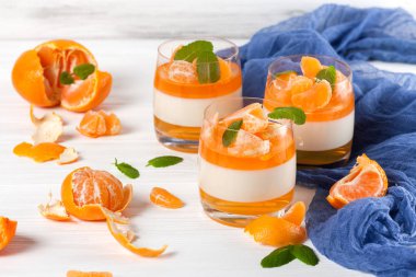 Güzel gözlük, taze olgun mandarin, Beyaz ahşap zemin üzerinde mavi tekstil turuncu jöle ile kremsi panna cotta. Lezzetli İtalyan tatlı. Portre fotoğrafçılığı. Seçici odak.