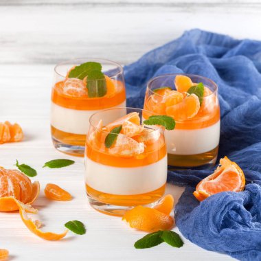 Güzel gözlük, taze olgun mandarin, Beyaz ahşap zemin üzerinde mavi tekstil turuncu jöle ile kremsi panna cotta. Lezzetli İtalyan tatlı. Portre fotoğrafçılığı. Seçici odak.