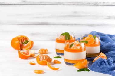 Güzel gözlük, taze olgun mandarin, Beyaz ahşap zemin üzerinde mavi tekstil turuncu jöle ile kremsi panna cotta. Lezzetli İtalyan tatlı. Portre fotoğrafçılığı. Seçici odak.