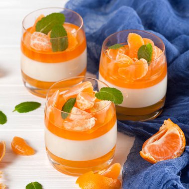 Güzel gözlük, taze olgun mandarin, Beyaz ahşap zemin üzerinde mavi tekstil turuncu jöle ile kremsi panna cotta. Lezzetli İtalyan tatlı. Portre fotoğrafçılığı. Seçici odak.