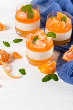 Güzel gözlük, taze olgun mandarin, Beyaz ahşap zemin üzerinde mavi tekstil turuncu jöle ile kremsi panna cotta. Lezzetli İtalyan tatlı. Portre fotoğrafçılığı. Seçici odak.