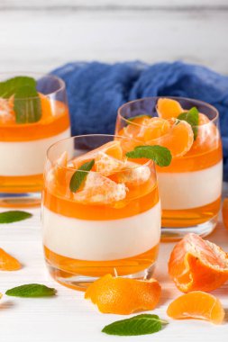 Güzel gözlük, taze olgun mandarin, Beyaz ahşap zemin üzerinde mavi tekstil turuncu jöle ile kremsi panna cotta. Lezzetli İtalyan tatlı. Portre fotoğrafçılığı. Seçici odak.