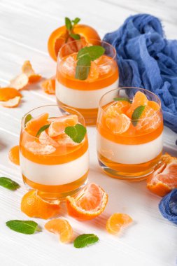 Güzel gözlük, taze olgun mandarin, Beyaz ahşap zemin üzerinde mavi tekstil turuncu jöle ile kremsi panna cotta. Lezzetli İtalyan tatlı. Portre fotoğrafçılığı. Seçici odak.