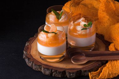 Kremsi panna cotta ile güzel bardaklarda portakal jöle, taze olgun mandarin siyah arka plan üzerine ahşap bölümünde. Lezzetli İtalyan tatlı. Modern karanlık ruh stili.