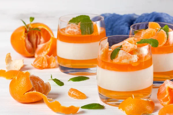Güzel gözlük, taze olgun mandarin, Beyaz ahşap zemin üzerinde mavi tekstil turuncu jöle ile kremsi panna cotta. Lezzetli İtalyan tatlı. Portre fotoğrafçılığı. Seçici odak.