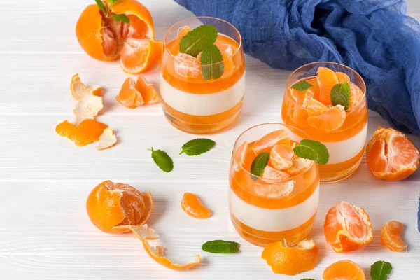 Smetanové panna cotta s oranžové želé v krásné brýle, čerstvé zralé mandarinky, modré textilní na bílém pozadí dřevěná. Italský zákusek. Detailní fotografie. Selektivní fokus. — Stock fotografie