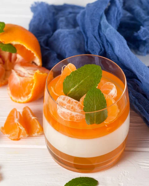 Güzel gözlük, taze olgun mandarin, Beyaz ahşap zemin üzerinde mavi tekstil turuncu jöle ile kremsi panna cotta. Lezzetli İtalyan tatlı. Portre fotoğrafçılığı. Seçici odak.