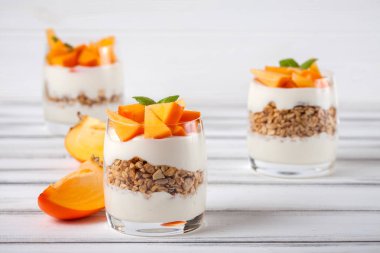 Trabzon hurması kremalı pasta ister güzel gözlük, taze olgun meyve dilimleri Beyaz ahşap zemin üzerinde. Sağlıklı vejetaryen yemek. Lezzetli tatlı. Fotoğraf kadar kapatın. Seçici odak.