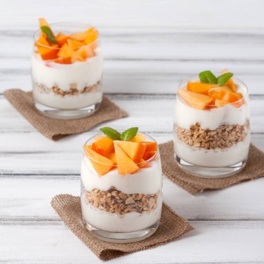 Trabzon hurması kremalı pasta ister güzel gözlük, taze olgun meyve dilimleri Beyaz ahşap zemin üzerinde. Sağlıklı vejetaryen yemek. Lezzetli tatlı. Fotoğraf kadar kapatın. Seçici odak.