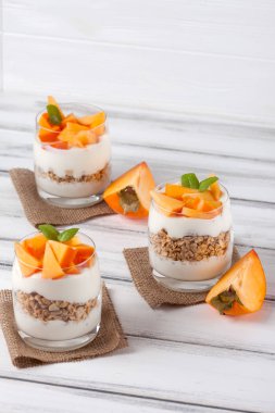 Trabzon hurması kremalı pasta ister güzel gözlük, taze olgun meyve dilimleri Beyaz ahşap zemin üzerinde. Sağlıklı vejetaryen yemek. Lezzetli tatlı. Fotoğraf kadar kapatın. Seçici odak.