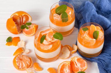 Güzel gözlük, taze olgun mandarin, Beyaz ahşap zemin üzerinde mavi tekstil turuncu jöle ile kremsi panna cotta. Lezzetli İtalyan tatlı. Portre fotoğrafçılığı. Seçici odak.