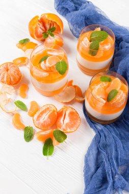 Güzel gözlük, taze olgun mandarin, Beyaz ahşap zemin üzerinde mavi tekstil turuncu jöle ile kremsi panna cotta. Lezzetli İtalyan tatlı. Portre fotoğrafçılığı. Seçici odak.