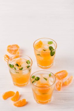 Mandarin buz ve güzel gözlük ve sürahi, Beyaz ahşap zemin üzerinde olgunlaşmış taze narenciye nane kokteyli. Tatlı portakal suyu. Fotoğraf kadar kapatın. Seçici odak