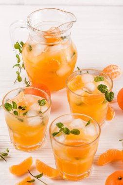 Mandarin buz ve güzel gözlük ve sürahi, Beyaz ahşap zemin üzerinde olgunlaşmış taze narenciye nane kokteyli. Tatlı portakal suyu. Fotoğraf kadar kapatın. Seçici odak