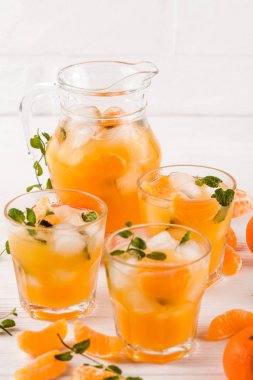 Mandarin buz ve güzel gözlük ve sürahi, Beyaz ahşap zemin üzerinde olgunlaşmış taze narenciye nane kokteyli. Tatlı portakal suyu. Fotoğraf kadar kapatın. Seçici odak