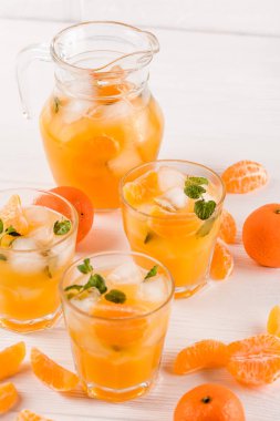 Mandarin buz ve güzel gözlük ve sürahi, Beyaz ahşap zemin üzerinde olgunlaşmış taze narenciye nane kokteyli. Tatlı portakal suyu. Fotoğraf kadar kapatın. Seçici odak