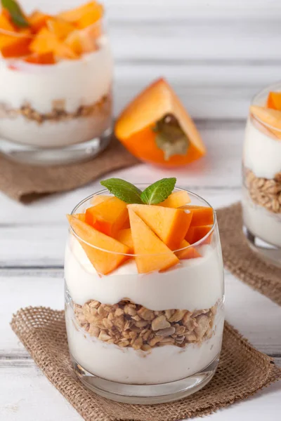 Persimmon creamy trifle in beautiful glasses, fresh ripe fruit slices on white wooden background. Healthy vegetarian food. Delicious dessert. Close up photography. Selective focus. — Stock Photo, Image