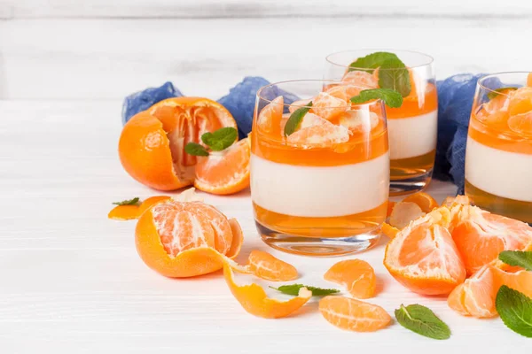 Smetanové panna cotta s oranžové želé v krásné brýle, čerstvé zralé mandarinky, modré textilní na bílém pozadí dřevěná. Italský zákusek. Detailní fotografie. Selektivní fokus. — Stock fotografie