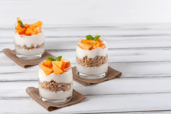 Persimon krämig bagatell i vackra glas, färska mogna frukt skivor på vit trä bakgrund. Hälsosam vegetarianmat. Läcker dessert. Närbild av fotografi. Selektivt fokus. — Stockfoto