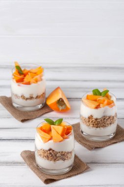 Trabzon hurması kremalı pasta ister güzel gözlük, taze olgun meyve dilimleri Beyaz ahşap zemin üzerinde. Sağlıklı vejetaryen yemek. Lezzetli tatlı. Fotoğraf kadar kapatın. Seçici odak.